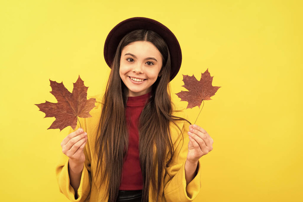 自然の美しさ。秋のファッション。帽子の10代の女の子は紅葉を持っています。黄色の背景にカエデの葉で楽しい子供。秋の自然。子供の頃の幸せ. - 写真・画像