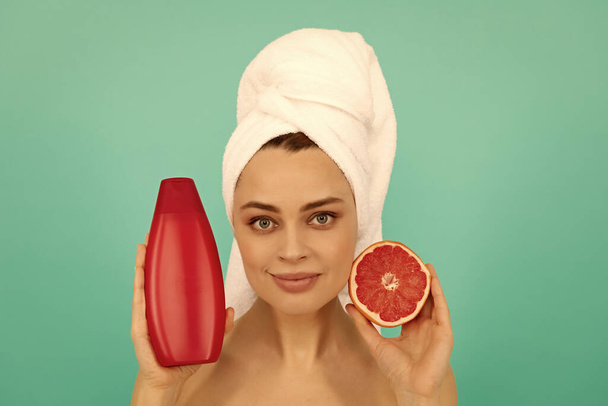 обличчя молодої жінки в рушнику з пляшкою шампуню з грейпфрутом на синьому фоні
. - Фото, зображення