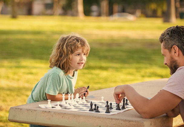 happy family of dad and son boy playing chess on table in park outdoor, chess competition. - Fotografie, Obrázek