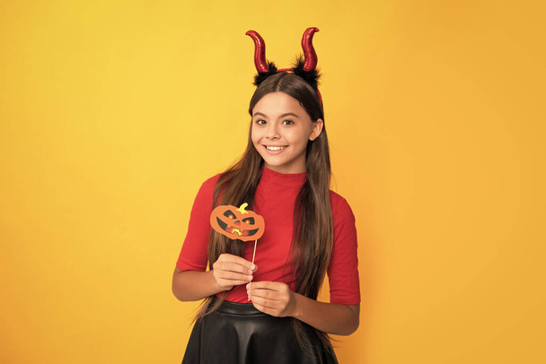happy kid with pumpkin party accessory wearing devil horns on yellow background, happiness. - Fotó, kép