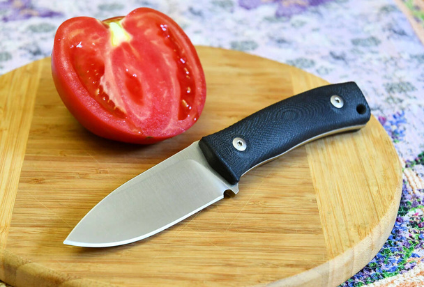 Knife cutting edge black handle red fresh sliced tomato delicious fetus cooking food wooden plate green background - Foto, afbeelding