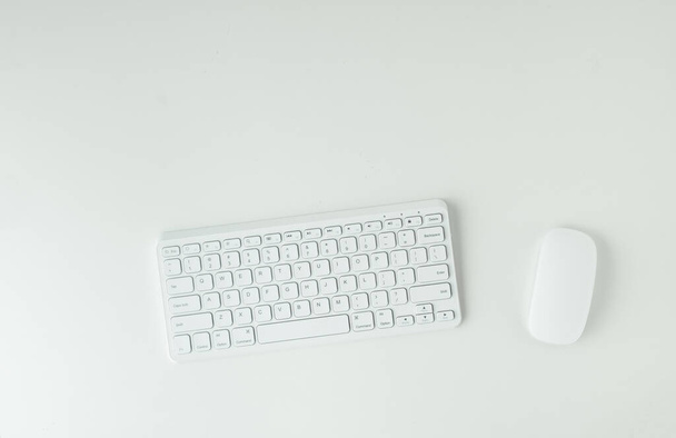 White GWERTY keyboard and mouse on the white table surface. Working place concept. Flat lay of office desk. Copy space for a text - Foto, Bild
