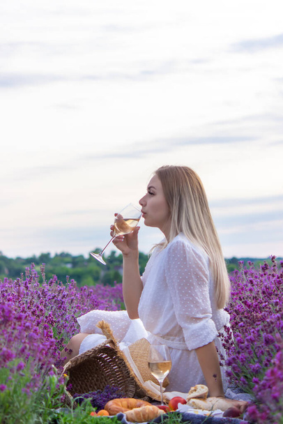 a girl holds a glass of white wine against the backdrop of a lavender field. A girl drinks wine in a lavender field. selective focus - Foto, Imagem