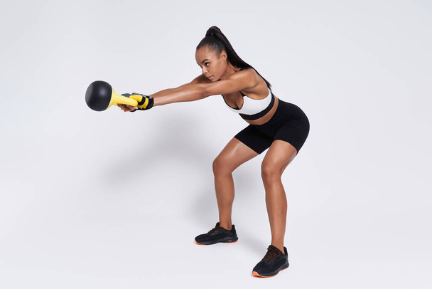 Confident young African woman exercising with kettlebell against white background - Photo, Image