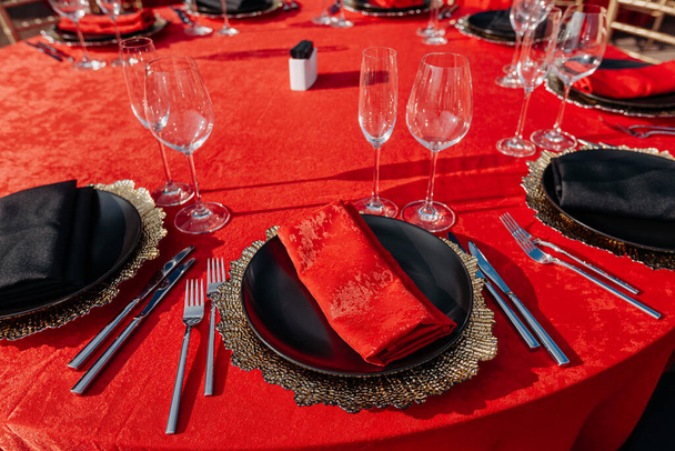 Apparecchiatura tavola per banchetti in stile nero, rosso e oro. Cena elegante e di lusso: arredamento, tovaglia, piatti, bicchieri, tovaglioli, posate. Festa di compleanno o di nozze a tema - Foto, immagini