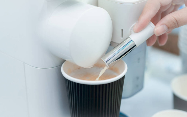 Woman making a cup of hot coffee with capsule coffee machine. Woman hand holding frothed milk dispenser of capsule coffee machine on table. Latte coffee maker. Morning drink. Modern home equipment. - Zdjęcie, obraz