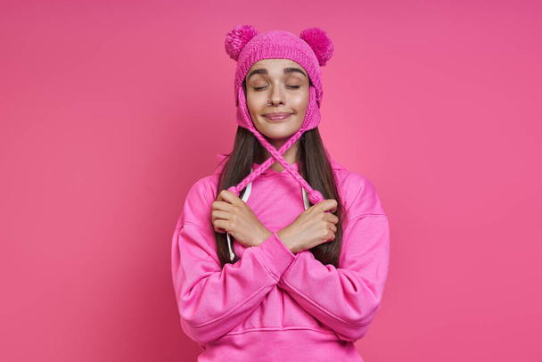 Playful young woman in hooded shirt adjusting her funky hat against pink background - Фото, зображення
