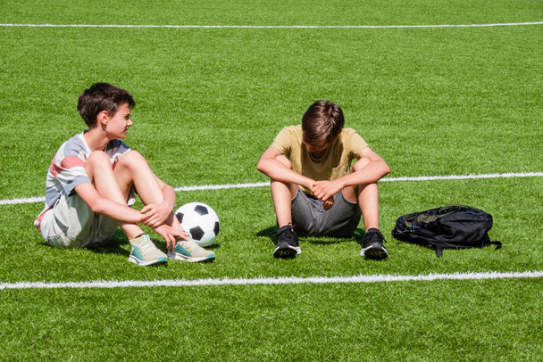 Children talking in school stadium outdoors. Teenage boy comforting consoling upset sad friend. Education, bullying, conflict, social relations, problems at school, learning difficulties concept. - Photo, Image