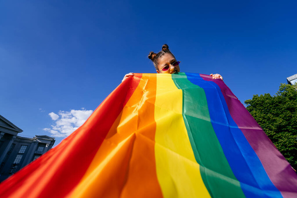 Una giovane donna sviluppa una bandiera arcobaleno contro il cielo a sostegno della comunità LGBT - Foto, immagini