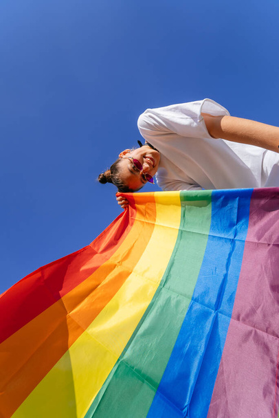 Una giovane donna sviluppa una bandiera arcobaleno contro il cielo a sostegno della comunità LGBT - Foto, immagini