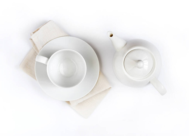 White teapot and empty teacup on pale beige cloth isolated on white background. Flat lay, top view - Foto, Imagen