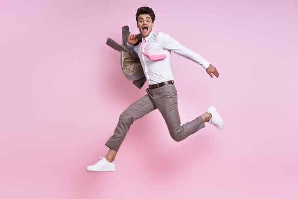 Happy man in shirt and tie carrying jacket on shoulder while jumping against pink background - Foto, Bild