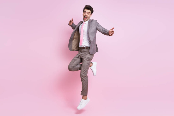 Happy young man in full suit jumping against pink background - Фото, зображення