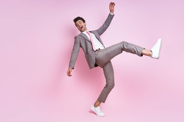 Excited young man in full suit moving against pink background - Photo, image