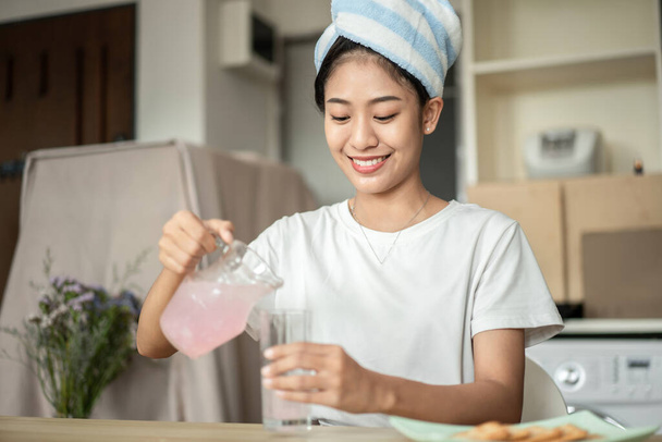 Half Asian woman drinking juice and eating crackers (Healthy whole grain)  for breakfast before going to work, Small room in condominium background, Wake-up activities. - Foto, Imagen