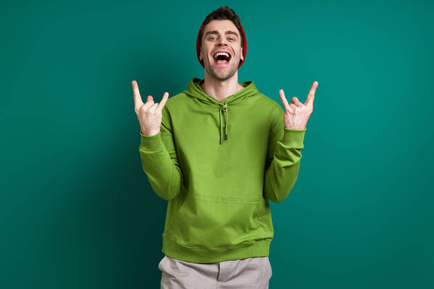 Handsome young man gesturing and smiling while standing against green background - Φωτογραφία, εικόνα
