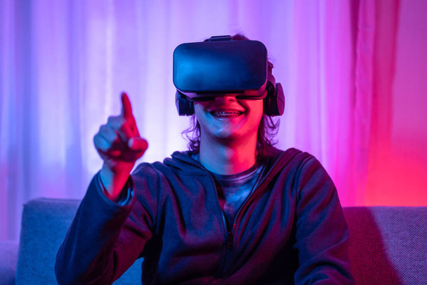 Молодий чоловік в окулярах віртуальної реальності (VR) грає в ігри в кімнаті з червоним і синім світлом, грає в 3D гру з хвилюванням, майбутні ігри, гаджети, технології, концепція гри VR
. - Фото, зображення