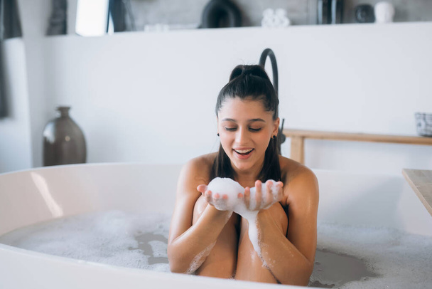 Молодая женщина, наслаждаясь расслабленной пеной ванны в интерьере дома - Фото, изображение