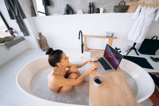 Mujer joven que trabaja en el ordenador portátil mientras toma una bañera en casa - Foto, imagen