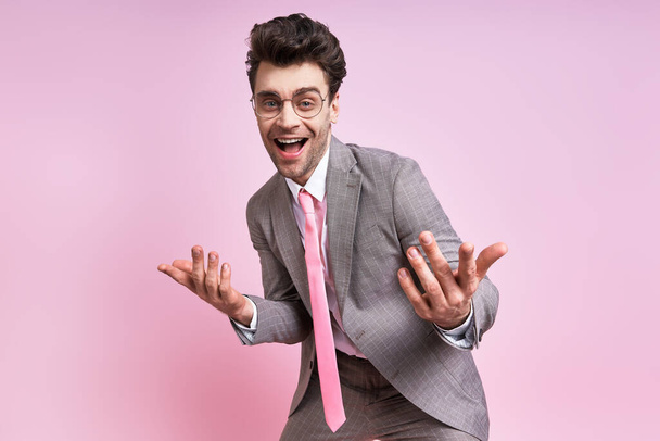 Happy young man in full suit gesturing while standing against pink background - Foto, imagen