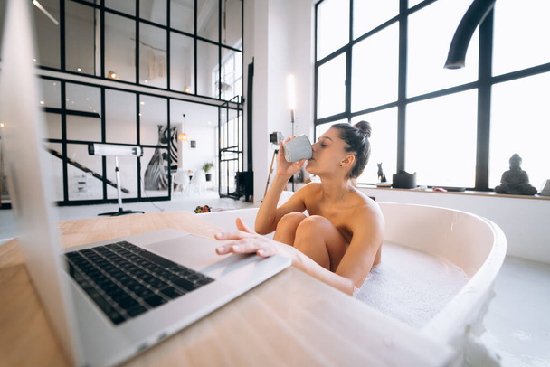 Молода жінка працює на ноутбуці, приймаючи ванну вдома
 - Фото, зображення