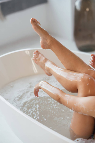 Cropped view of young woman lying in foamy bath, demonstrating silky skin on her legs - Foto, Imagen