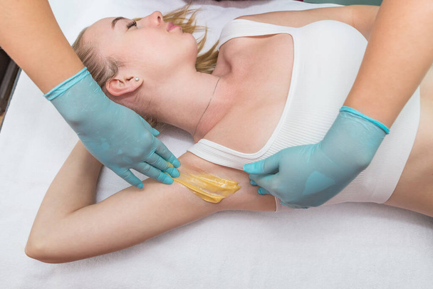 Depilation and epilation of the female armpit with liquid sugar paste. The beautician's hand applies wax paste to the armpit. The concept of smooth armpits - Photo, image