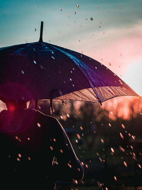 A male with an umbrella walking in the rain at sunset - Photo, image