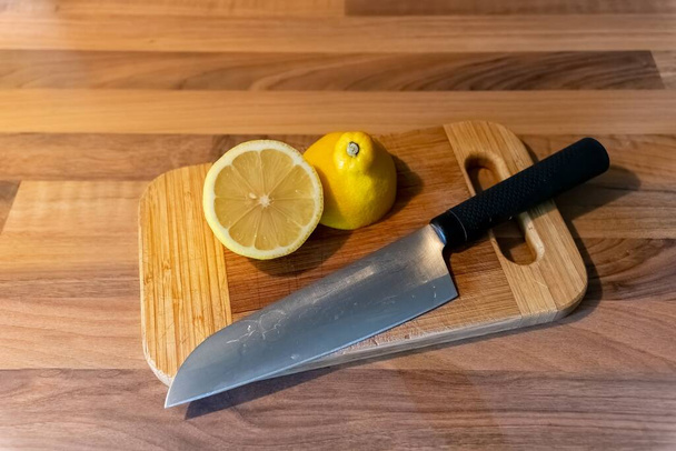 Two pieces of half-cut lemon lying on a wooden cutting board next to a knife - a healthy cooking concept - Foto, Bild