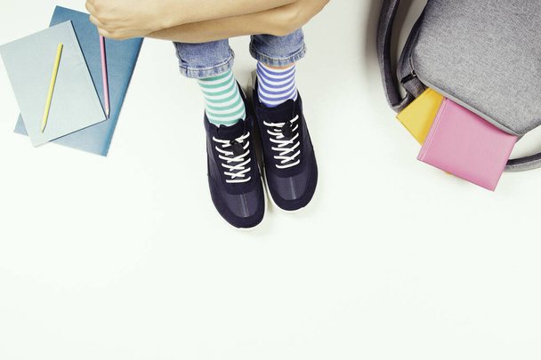 Kid wearing different pair of socks. Child in mismatched socks and colorful sneakers sitting on white background, with backpack, books and school supplies. Top view. - Foto, afbeelding
