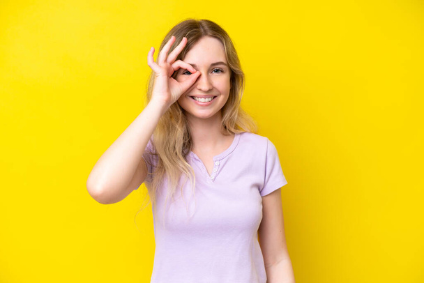 Blonde English young girl isolated on yellow background showing ok sign with fingers - Foto, immagini