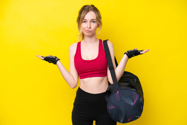 Young sport caucasian woman with sport bag isolated background having doubts while raising hands - Foto, Bild