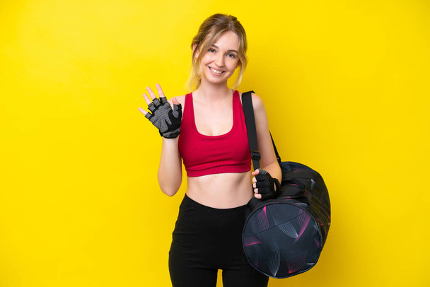 Young sport caucasian woman with sport bag isolated background saluting with hand with happy expression - Foto, Imagen