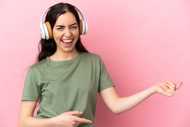 Young caucasian woman isolated on pink background listening music and doing guitar gesture - 写真・画像