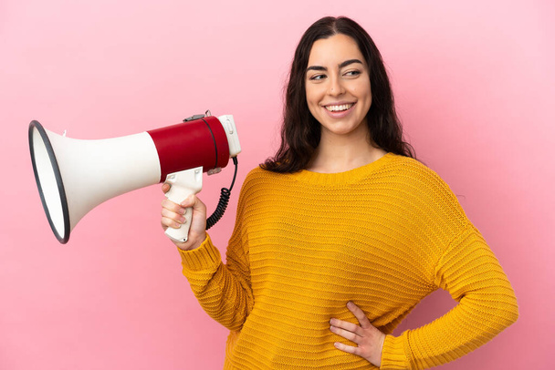Young caucasian woman isolated on pink background holding a megaphone and thinking - Foto, imagen
