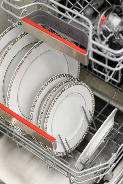 Open dishwasher with clean dishes in a white kitchen. Clean plates, cups and dishes. Nobody. Selective focus. - Photo, Image