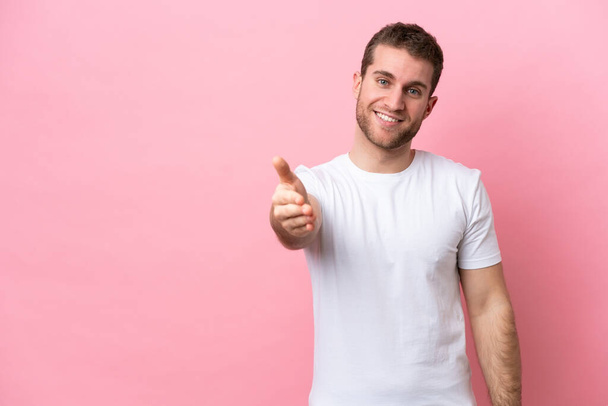 Young caucasian man isolated on pink background shaking hands for closing a good deal - Photo, Image