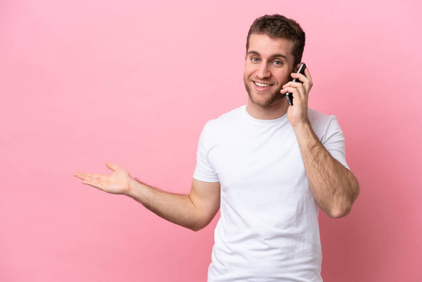 Joven hombre caucásico aislado sobre fondo rosa manteniendo una conversación con el teléfono móvil con alguien - Foto, imagen