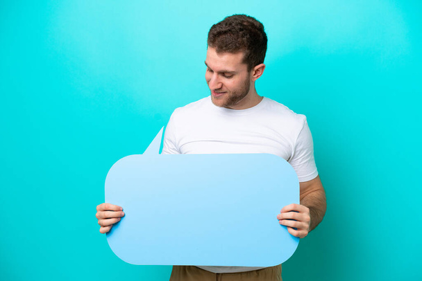 Young caucasian man isolated on blue background holding an empty speech bubble - Photo, Image
