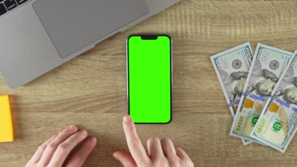 Scrolling the pages on the phone with green screen mockup. 100 dollar bills on the table. - 映像、動画