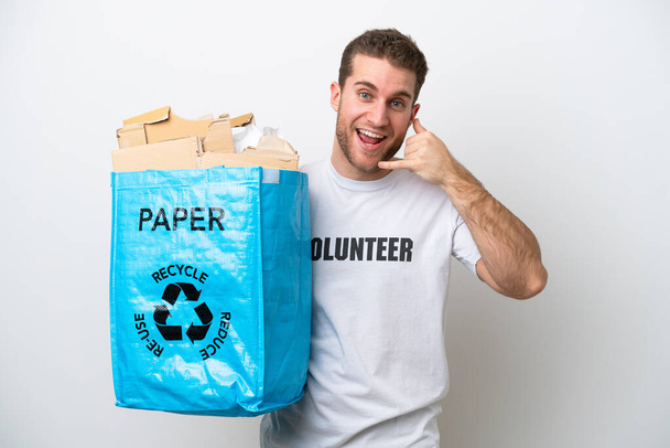 Νεαρός καυκάσιος που κρατάει μια σακούλα ανακύκλωσης γεμάτη χαρτί για να ανακυκλώνει απομονωμένος σε λευκό φόντο κάνοντας τηλεφωνική χειρονομία. Πάρε με τηλέφωνο. - Φωτογραφία, εικόνα