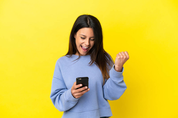 Young caucasian woman isolated on yellow background surprised and sending a message - Zdjęcie, obraz