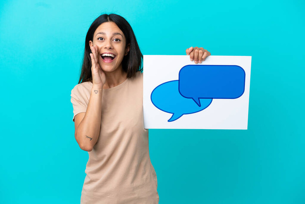Young woman over isolated background holding a placard with speech bubble icon and shouting - Foto, Bild