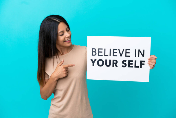 Young woman over isolated background holding a placard with text Believe In Your Self and pointing it - Photo, Image