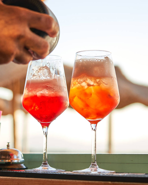 Spritz traditional cocktail with alcohol being prepared by unrecognizable man in a beach bar. European summer drink. Italian drink. Lifestyle concept - Фото, изображение