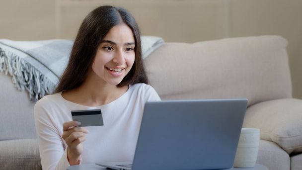 Happy female arabian consumer shopper hold plastic banking card enter numbers for online bank app pay money deposit use credit limit donate for charity transfer electronic savings for delivery service - Foto, imagen