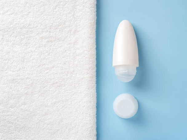 Roll on antiperspirant deodorant over blue background next to white bath towel with copy space. Purity, body care, toiletries and personal hygiene items concept. Cosmetic product mockup. Closeup. - Foto, Imagen