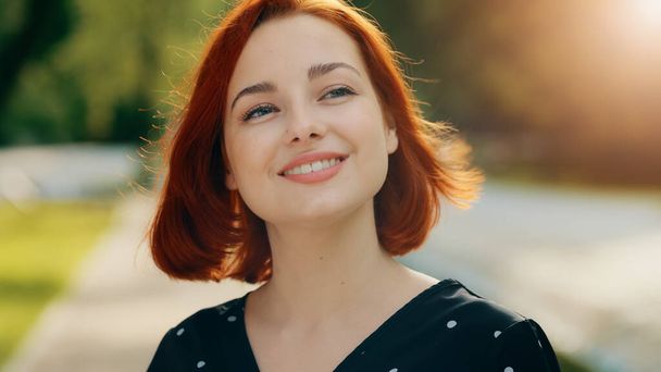 Inspired redhead female model woman attractive girl caucasian young lady inhaling fresh air make deep breath enjoying of blowing spring breeze looking at bright sun shining background fix hair smiling - Photo, image