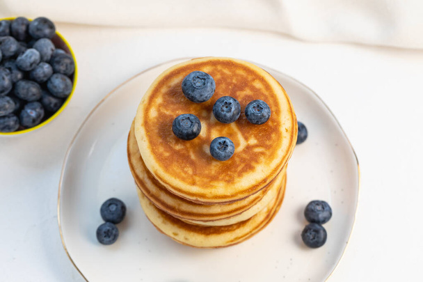 Stack of delicious pancakes on white plate with fresh blueberries on and in bowl. Top view, Copy space - 写真・画像