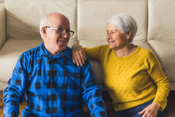 Розслаблена красива любляча старша сімейна пара дивиться один на одного, посміхаючись і активно обговорюючи щось, сидячи на підлозі біля дивана у вітальні вдома. Високоякісна фотографія
 - Фото, зображення